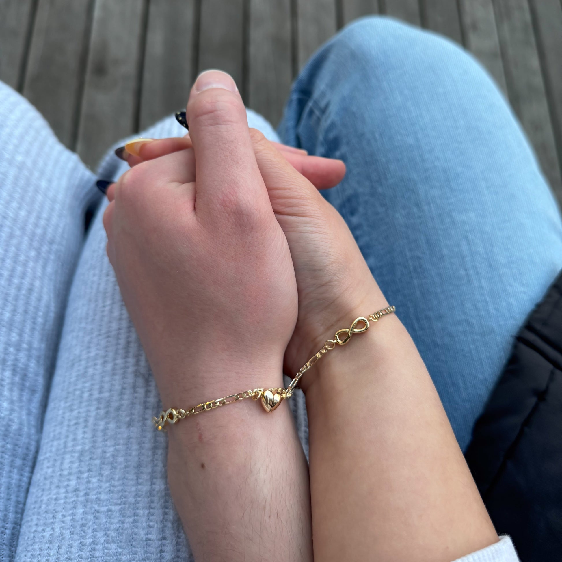 Two hands interlocked with gold bracelets on a wooden surface.